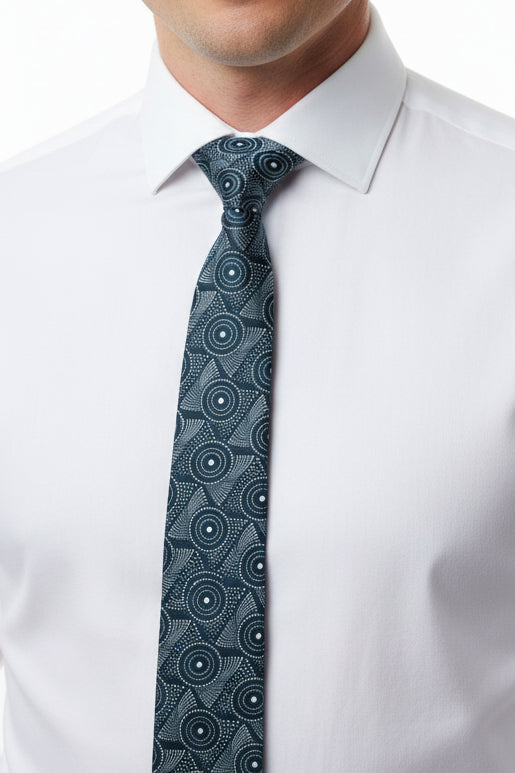 A slim necktie with a black and gray geometric circular pattern, laid flat on a light-colored wood plank surface.