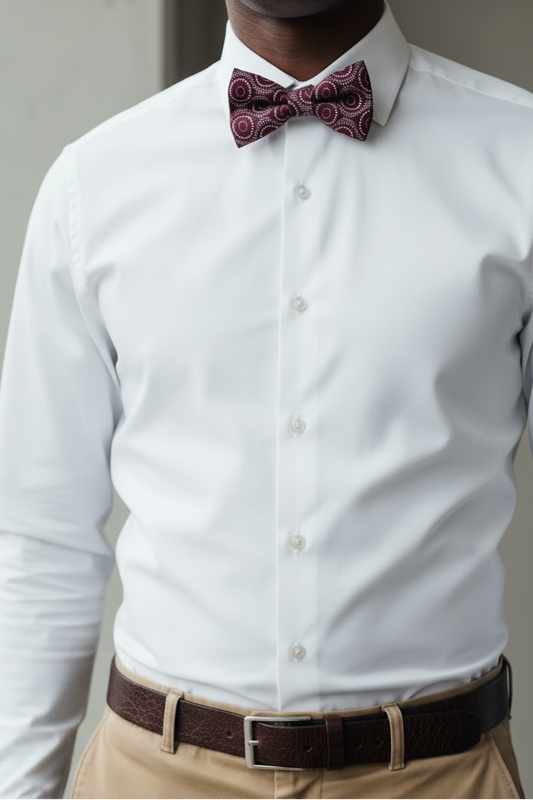 A man wearing a white long-sleeve dress shirt, khaki trousers, a dark brown belt, and a burgundy patterned bow tie, shown from the neck down in a clean indoor setting.
