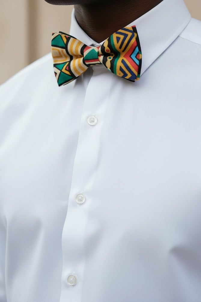 A pre-tied bow tie featuring a vibrant, multicolored geometric pattern with yellow, teal, red, black, and cream, displayed flat against a light gray background.